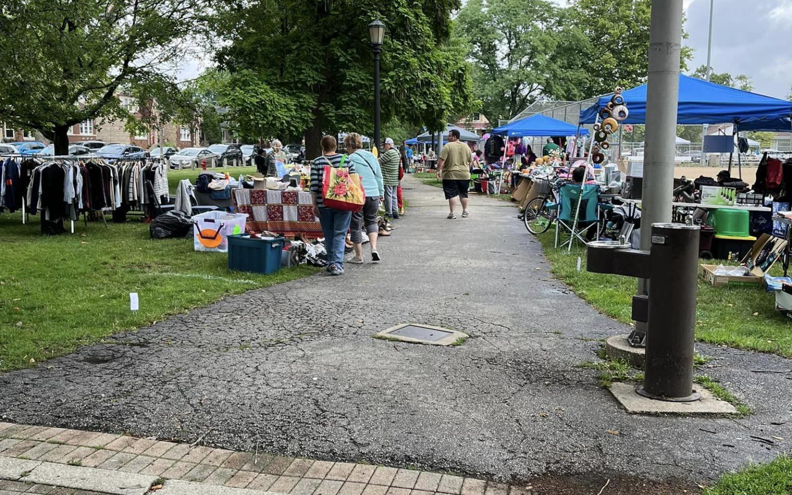 People walking down the path at Proksa Park viewing items in tents for the community garage sale