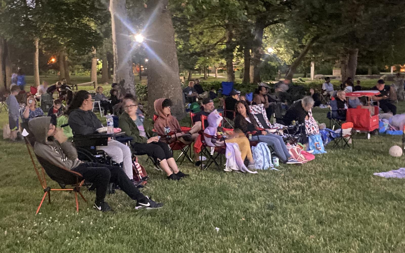 an image of people in lawn chairs sitting with neighbors to enjoy movies in the park