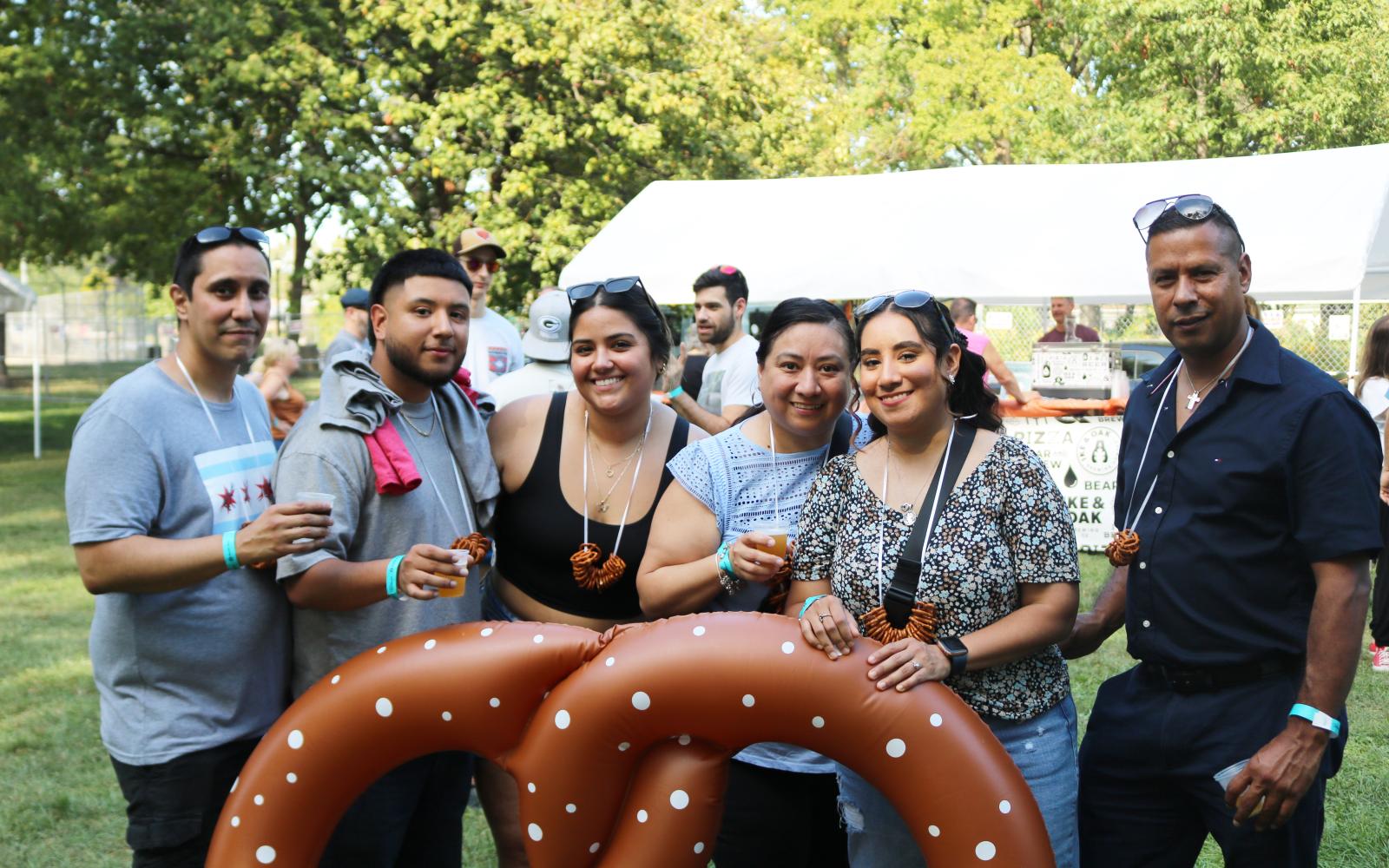 An image of a group of friends at Berwyn Brewfest posing around an inflatable pretzel with brews in-hand