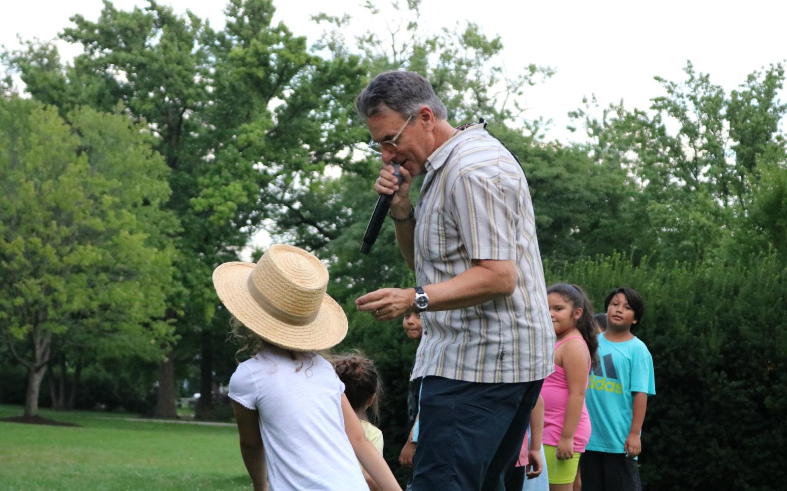 An image of lead singer with a microphone singing with a group full of children