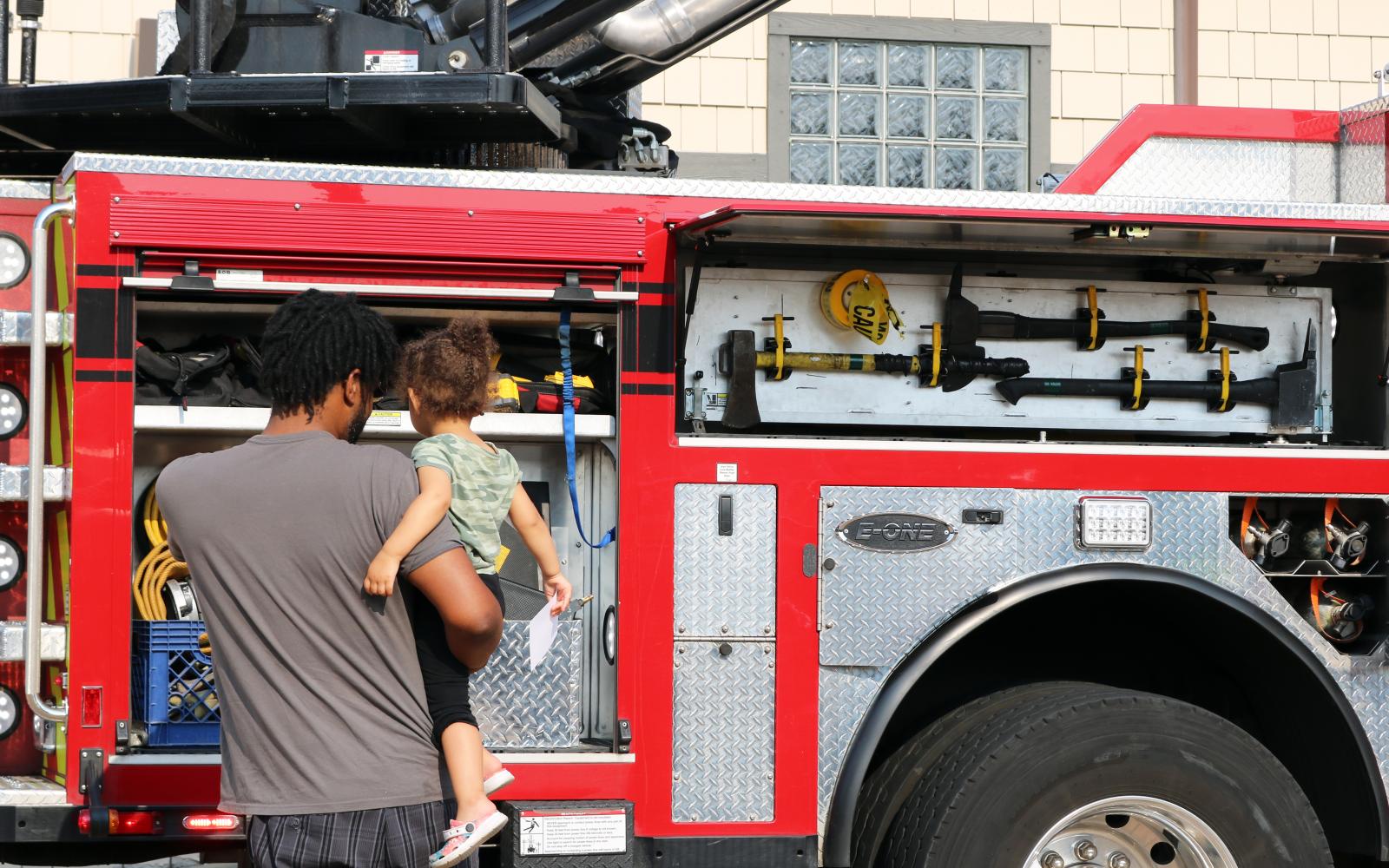 A photo of a man holding a child and pointing at the side of a fire truck