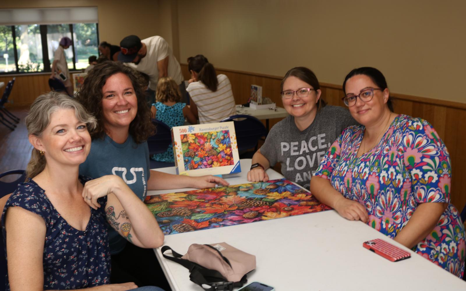A photo of  a group of four people seated around a table with a completed puzzle