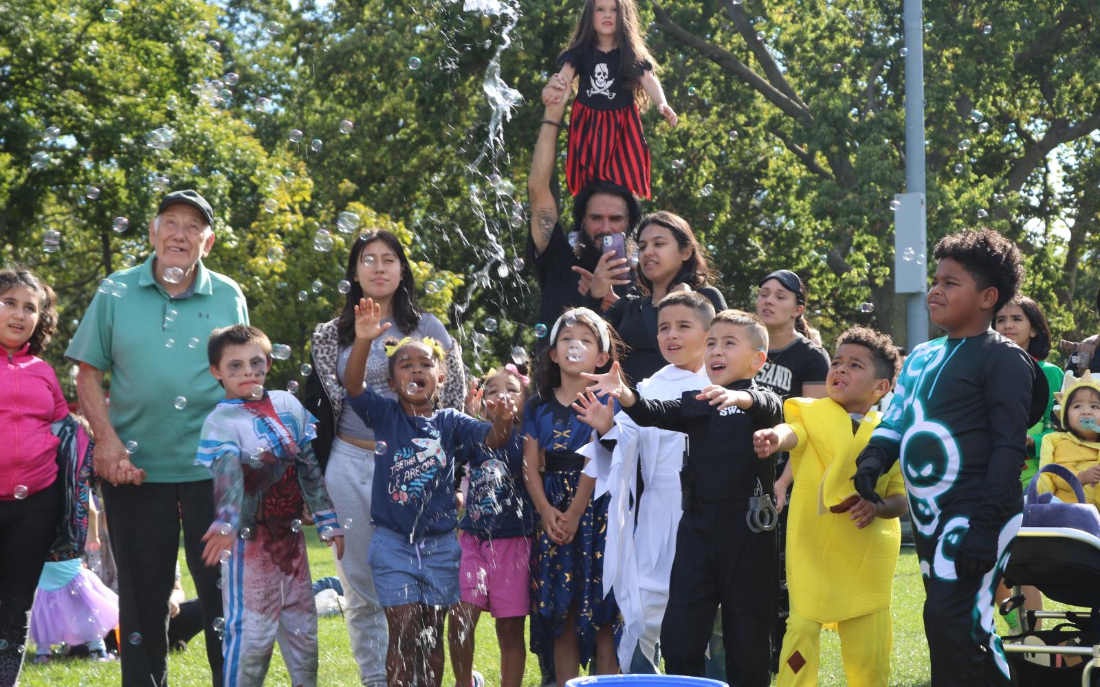 kids and adults in various halloween costumes gathered around bubbles