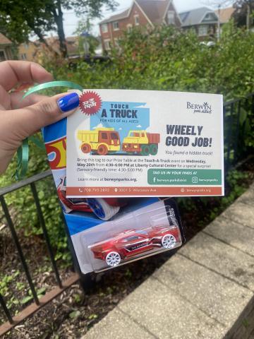 An image of a hand with a blue fingernail holding a hot wheels car and a tag that states that they found a hidden truck Bring this tag to our Prize Table at the Touch-A-Truck event on Wednesday, May 20th from 4:30–6:00 PM at Liberty Cultural Center for a special surprise! (Sensory-friendly time: 4:30–5:00 PM) 